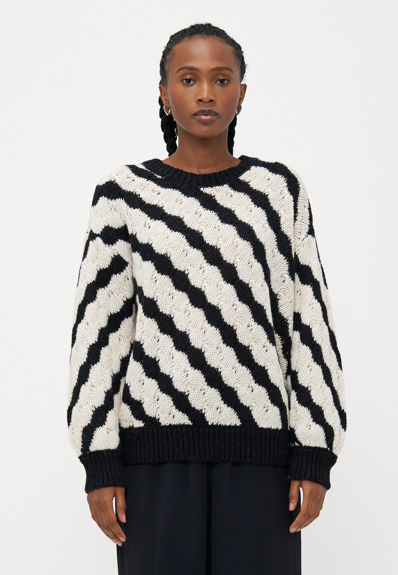 Maglione a maglia grossa in bianco e nero con righe a zig zag, scollatura rotonda e polsini e orlo a coste. Texture morbida, vestibilità oversize.