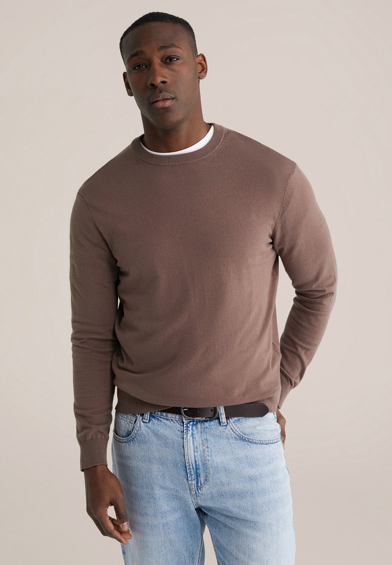 Pull léger marron à manches longues avec détails côtelés au niveau de l'encolure, associé à un jean bleu clair. Texture lisse avec des accents minimaux.