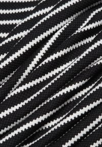 Stoff mit schwarz-weißen Streifen und gerippter Textur, der abwechselnd dünne weiße und dicke schwarze Streifen aufweist. Das Material erscheint weich und dehnbar.