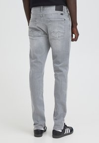 Bagfra set af person iført lysegrå jeans med baglommer og sorte sneakers med hvide striber, stående på en neutral baggrund.