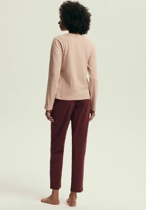 Jasnoróżowa koszula z długim rękawem w połączeniu z bordowymi, zwężanymi spodniami. Tkanina wydaje się miękka, z prostym, okrągłym dekoltem i bez widocznych wzorów.