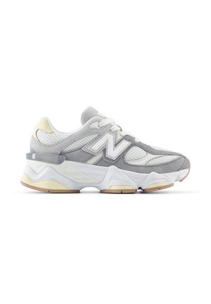Sneaker grigia e bianca con pannelli in rete, sovrapposizioni in suede, suola spessa e un logo "N" prominente sul lato.