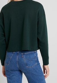 Ciemnozielona krótka bluza z długimi rękawami, zestawiona z jasnoniebieskimi, wysokim stanem jeansami o klasycznym kroju z pięcioma kieszeniami.