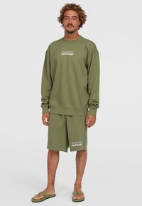 Olivenfarvet sweatshirt og shorts sæt lavet af blødt materiale, med en afslappet pasform og hvid "Surf Society" tekst på shortsen.