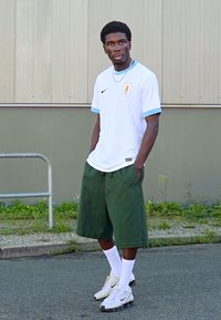 Hvid Nike fodboldtrøje med lyseblå accenter, grønne shorts, hvide sokker og lyse sneakers, sat mod en neutral baggrund.