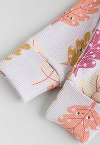 Ribbad långärmad plagg i ljuslila med ett bladmönster i rosa, gult och brunt. Har manschetter med matchande mönster.
