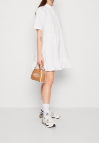 White, short-sleeve, button-up dress with a ruffled hem. Accessories include a small brown handbag and chunky white sneakers.