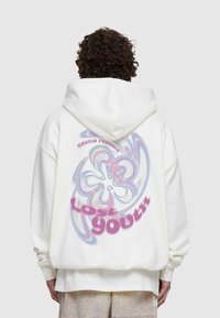 Vit oversized hoodie med en mångfärgad virvelgrafik och texten "Lost Youth" i rosa på baksidan. Blandning av bomull.
