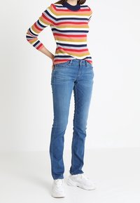 Suéter de punto con rayas horizontales multicolores; vaqueros azules; zapatillas blancas. Corte casual, textura acanalada, escote redondeado, diseño bien ajustado.