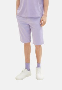 Shorts de algodón lavanda con bolsillos laterales, un ajuste relajado y un dobladillo justo por encima de la rodilla, combinados con zapatillas blancas y calcetines lilas.