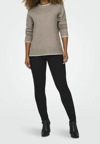 Brauner, gestrickter Pullover mit gewelltem weißen Saum an den Ärmeln und am unteren Rand, kombiniert mit schwarzen, engen Jeans und Ankle Boots. Glatte Textur.