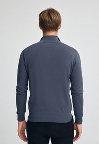 Grå tröja med hög krage, ribbade mudd och nederkant. Tillverkad av mjukt material, har en slät yta och en figurnära design.