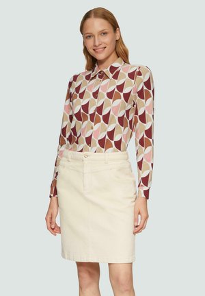 Langärmliges Hemd mit Knopfleiste und geometrischem Muster in Rot, Pink und Beige, kombiniert mit einem cremefarbenen Jeansrock.