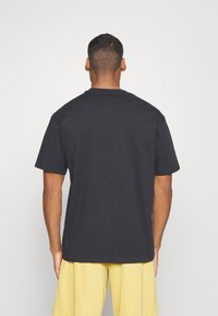 Camiseta de algodón negra con mangas cortas y cuello redondo, vista desde la parte posterior. Textura suave, corte relajado, sin gráficos ni patrones visibles.