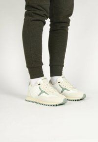 Witte sneakers met lichtgroene accenten, gemaakt van suede en mesh materialen, met een textuurzool en contrasterende veters, gecombineerd met donkere joggers.
