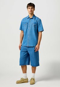 Lichtblauwe denim shirt met korte mouwen, drukknopen, twee borstzakken en contrasterende stiksels, gecombineerd met bijpassende blauwe denim shorts.