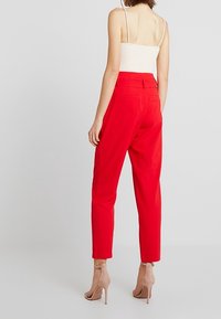 Pantalons rouges ajustés à taille haute, jambes fuselées et poches arrière ; associés à un haut crème ajusté et des chaussures à talons beiges.