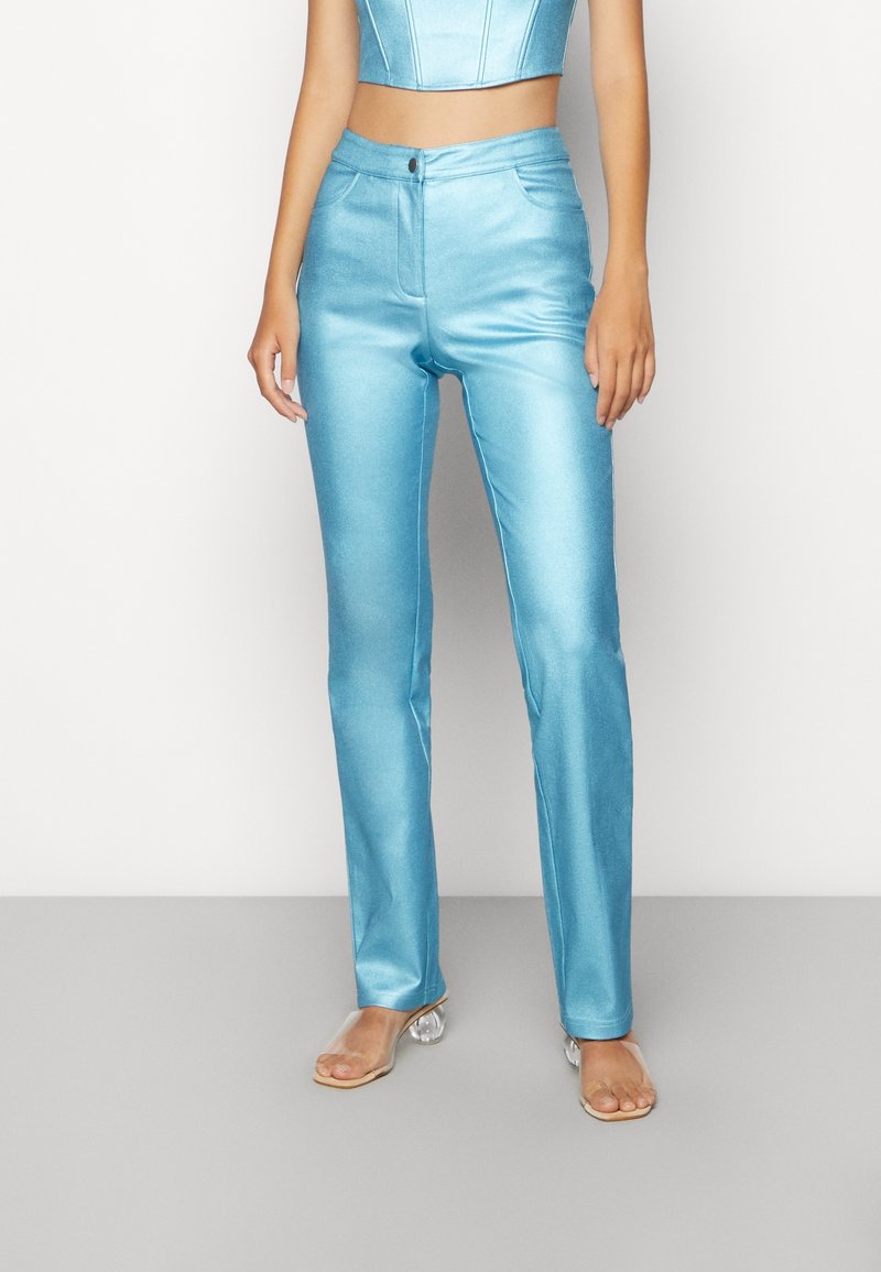 Satin blue pants with a fitted design, straight legs, front pockets, and a button closure. Transparent heeled sandals complete the look.