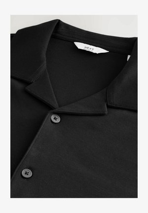 Schwarzes Poloshirt mit kurzen Ärmeln und umgeschlagenem Kragen, ausgestattet mit zwei schwarzen Knöpfen und einer glatten Textur. Etikett im Kragen sichtbar.