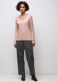 Långärmad V-ringad topp i mjuk rosa tyg, matchad med vida svarta och vita rutiga byxor. Modellen har på sig svarta ankelstövlar.