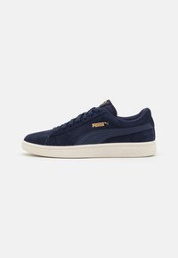 Navy mockasinsneakers med platta snören, kontrasterande krämfärgad gummisula och gyllene logotypdetaljer på sidan och tungan.