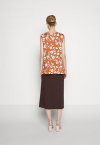 Blomtryckt topp i orange och vitt, ärmlös design, ihop med en brun knälång kjol, bärs med ljusa kraftiga klackar.