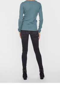 Světle modrý texturovaný top s dlouhými rukávy a kulatým výstřihem, kombinovaný s černými slim džíny a kotníkovými botami.