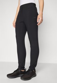 Svart träningsbyxor med en slät textur, tapered passform och en logotyp på sidan, kombinerat med svarta mesh-sneakers för en koordinerad look.