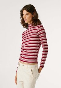 Rood en wit gestreepte langemouw turtleneck top, geribbeld textuur, aansluitend ontwerp, gecombineerd met lichtgekleurde broeken.