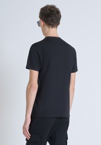 Camiseta negra de manga corta hecha de algodón. Diseño sencillo, cuello redondeado, textura suave, corte ajustado y sin patrones ni acentos visibles.