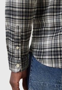 Grijs en zwart geruit overhemd met lange mouwen en knopenmanchetten, voorzien van een gestructureerde stof en een gebogen zoom, gecombineerd met blauwe denim.