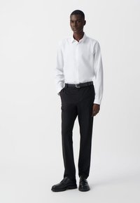 Witte overhemden met knopen, gecombineerd met zwarte broek en zwarte schoenen; gladde stof, op maat gemaakte pasvorm en minimalistisch ontwerp zonder patronen.