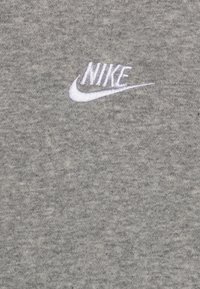 Camiseta de algodón gris con un logo de Nike bordado en blanco en el pecho. La tela tiene un acabado suave y texturizado.