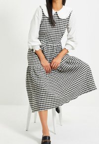 Svartvit rutig klänning med en åtsittande liv, utsvängd kjol och stor vit krage. Har långa ärmar med elastiska manschetter.