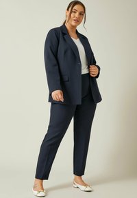 Marynarski żakiet o dopasowanym kroju i pasujące do niego spodnie wykonane z strukturalnej tkaniny. Biała bluzka, spiczaste białe baletki z złotymi akcentami oraz dopasowany krój.