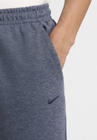 Pantalones de chándal azul marino en un tejido suave, con una cintura elástica y un bolsillo lateral; presenta un pequeño logotipo de Nike en azul oscuro en el muslo.