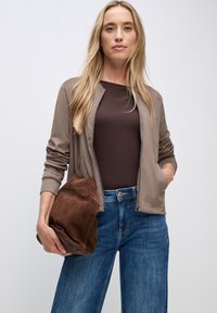 Ljus taupe zip-up bomberjacka med en slät yta, bärs över en mörkbrun topp och matchas med hög midja i blå denim. Håller en brun mockaväska.