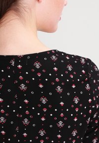 Tessuto nero con un piccolo motivo floreale in rosso e bianco. Collo rotondo e maniche corte, con una texture sottile e dettagli di cucitura.