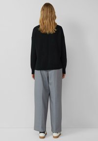 Schwarzer Strickpullover mit rundem Ausschnitt und geripptem Saum, kombiniert mit grauen, breitbeinigen Nadelstreifenhosen und weißen Turnschuhen.