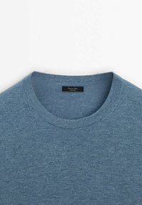 Pull bleu col rond en tissu tricoté doux, avec une étiquette de marque noire cousue à l'intérieur du col.