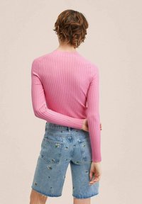 Różowa, prążkowana bluzka z długim rękawem w połączeniu z jasnoniebieskimi szortami dżinsowymi z haftem w kwiaty, prezentująca widok z tyłu oraz dopasowany krój.