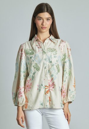 Blusa in lino beige con ricami floreali, dotata di maniche a sbuffo, chiusura frontale con bottoni e vivaci motivi floreali nei colori rosa, verde e blu.