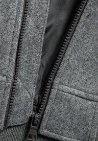 Grijze ritsjackdetail, dat een robuuste rits, gestikte patroon en textuurstof met een gladde zwarte binnenvoering toont.