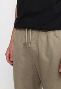 Beige trekbroek met een zachte textuur. Voorzien van een elastische tailleband en zijzakken. Gestyled met een zwart T-shirt met korte mouwen.