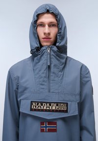 Lichtblauwe pulloverjas met een trekkoordkap, een rits aan de voorkant, geborduurd merkembleem en een patch met de Noorse vlag.