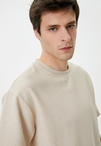 Beige strikket trøje med rund hals, korte ærmer og en struktureret overflade. Har en afslappet pasform og et minimalistisk design.