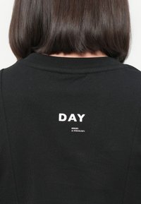 Black cotton T-shirt featuring a round neckline and white printed text on the back reading "DAY" above "BIRGER et MIKKELSEN."