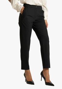 Pantaloni neri su misura con vestibilità slim, dotati di chiusura con bottone e tasche laterali. Il tessuto ha una texture liscia.