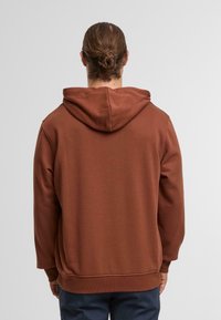 Brauner Kapuzenpullover mit weicher Textur und gerippten Bündchen, mit lässiger Passform und ohne sichtbare Logos oder Muster, von hinten betrachtet.