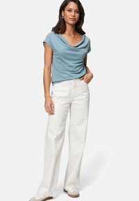 Light blue draped top with short sleeves paired with high-waisted white wide-leg trousers and casual white sneakers on a model.